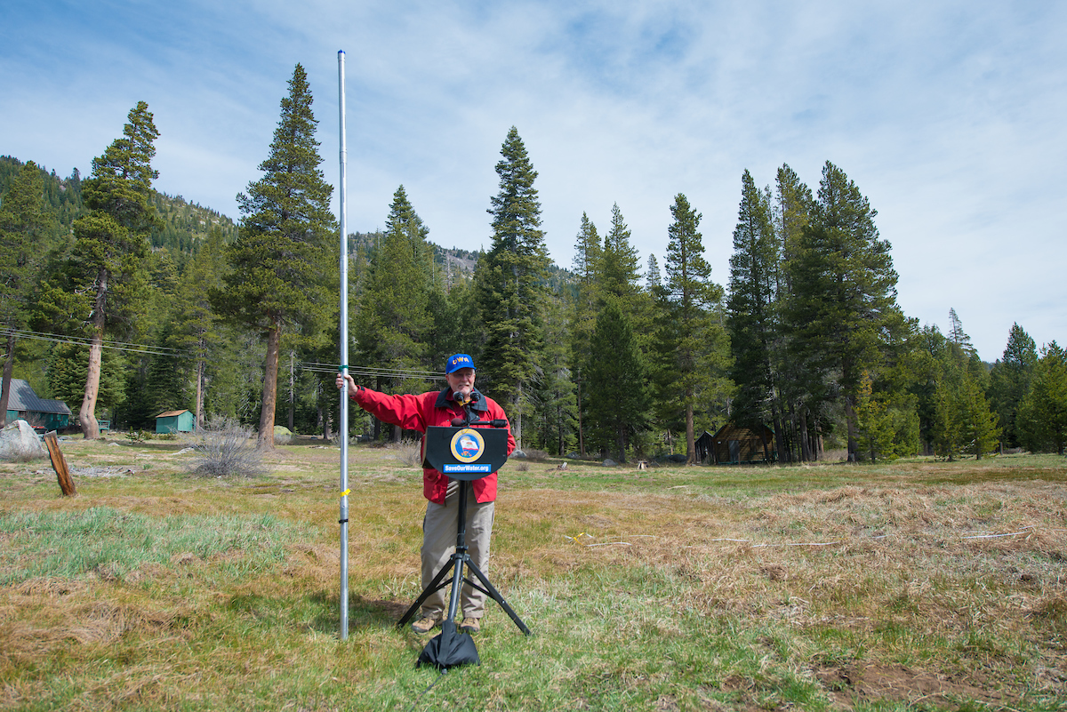 Frank Gehrke stands in a field with no snow holding the measuring pole.