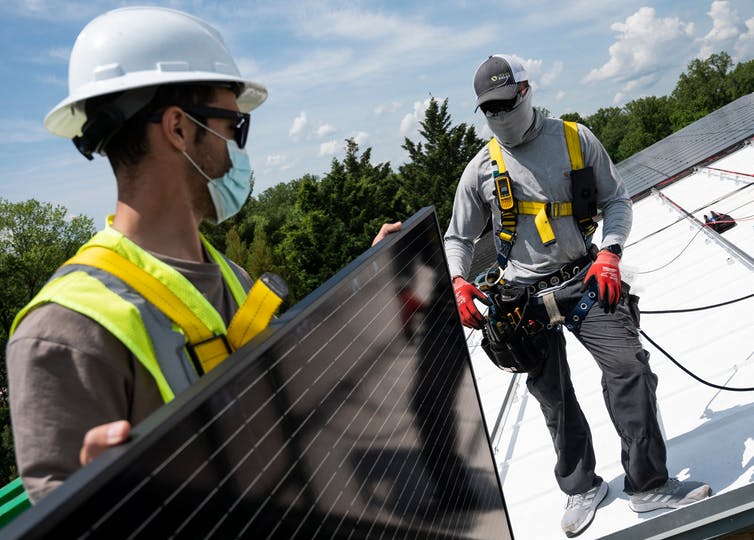 Two men standing on a slanted roof preparing to install a solar panel