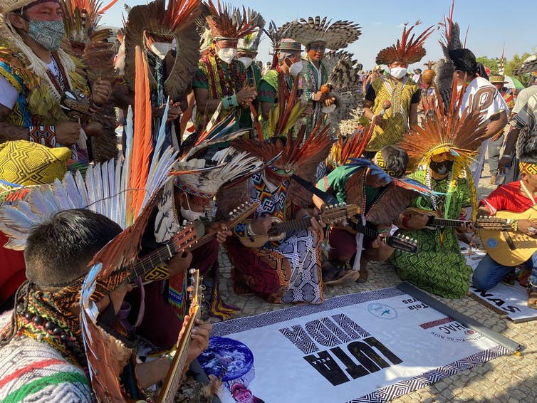 Amazonian Indigenous peoples in regalia surround a banner that says 'struggle for life.'