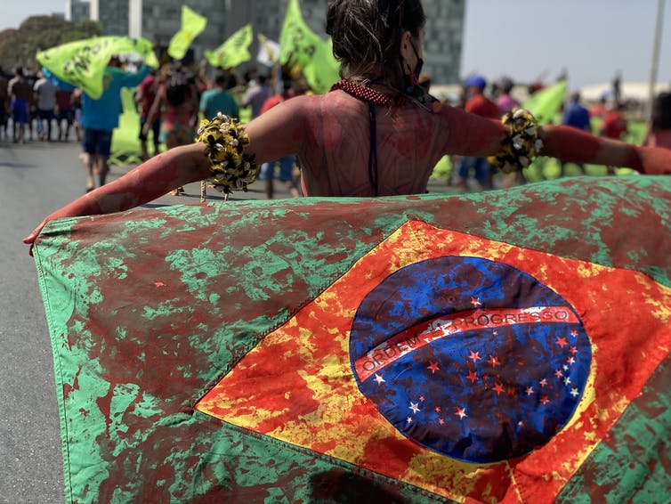 A woman is seen holding a flag covered in red paint.