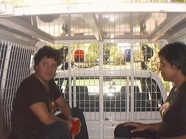 Two people in the back of a police paddywagon.