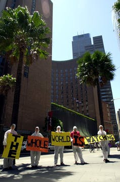 Protesters holding signs saying 'the whole world is watching'