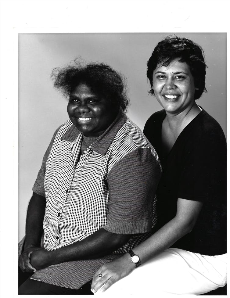 Two people sit smiling. The photo is in black and white.