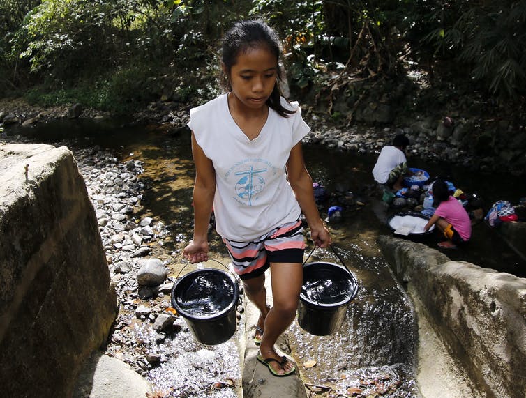 girl carries buckets of water from stream