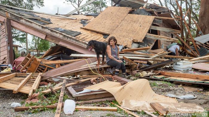 A woman with her dog sits in front of her destroyed house 