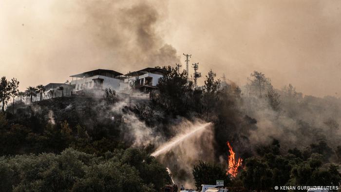Firefighters spray water to extinguish a fire approaching to a settlement near Cokertme village in Bodrum region, Turkey, August 3