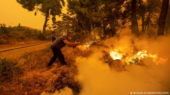 A man uses a tree branch to extinguish a wildfire burning in the village of Pefki, on the island of Evia, Greece, August 8, 2021