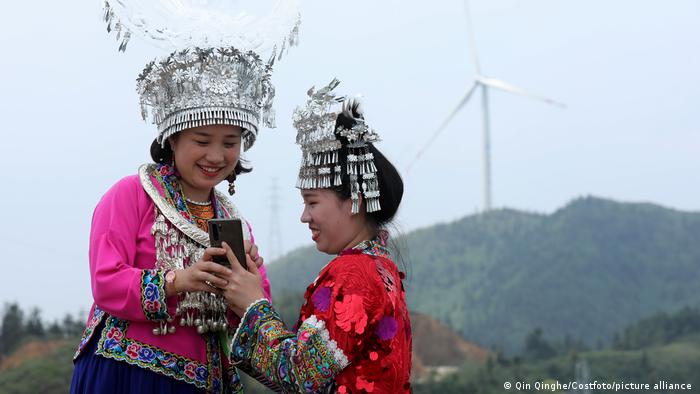 two women with headdress make selfie in front of wind turbine 