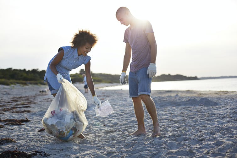 A man and woman pick up plastic waste on a beach.