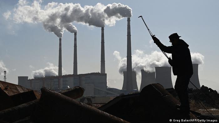 A worker cutting steel pipes against a backdrop of chimney stacks