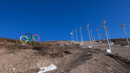 The Olympic rings appear on a ski hill that lacks snow.