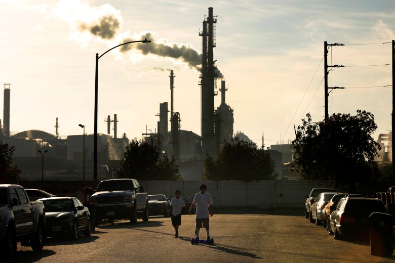 Kids on skateboards with refinery behind them.