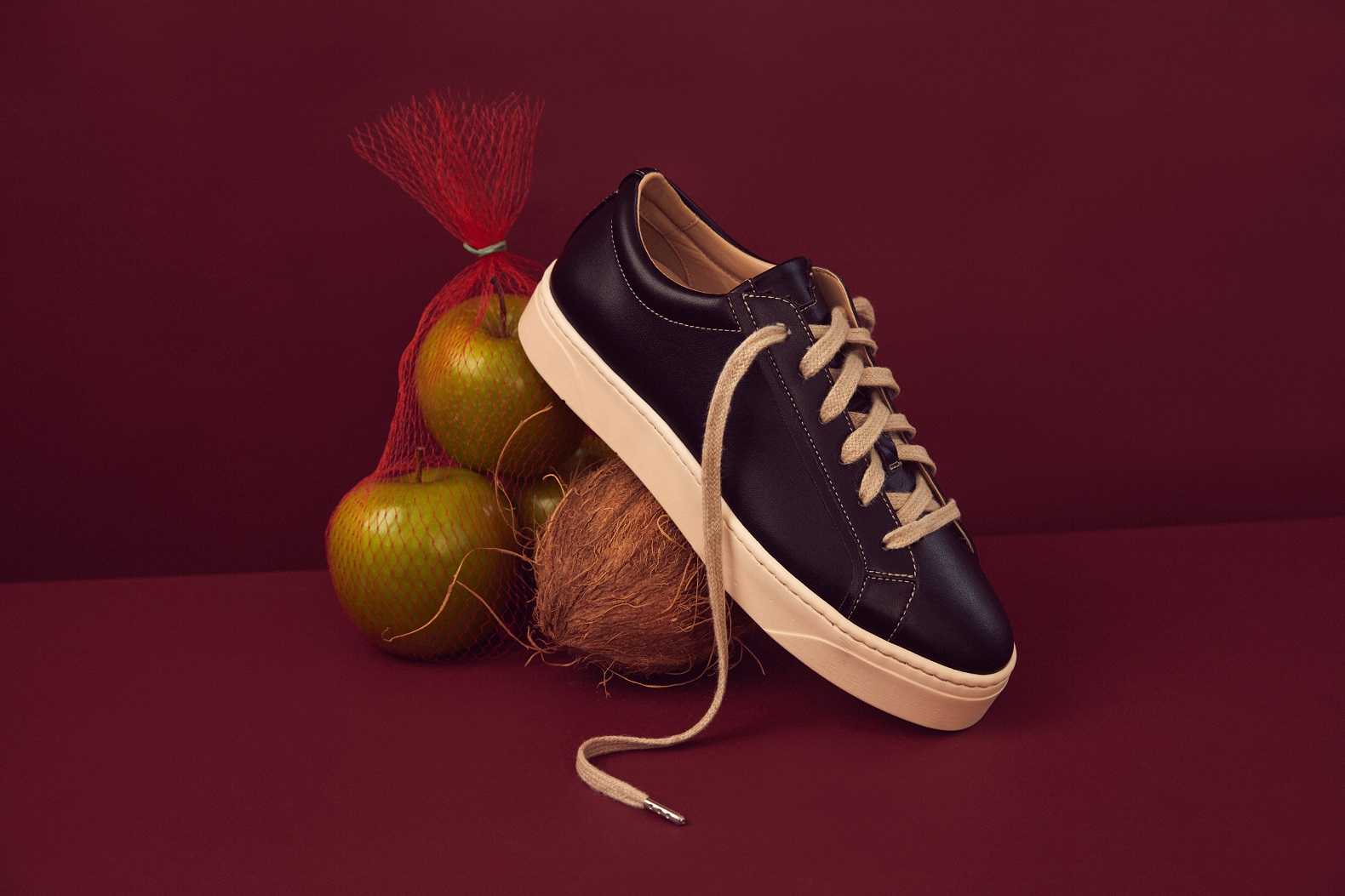 A black shoe with white laces leaning against a bag of apples