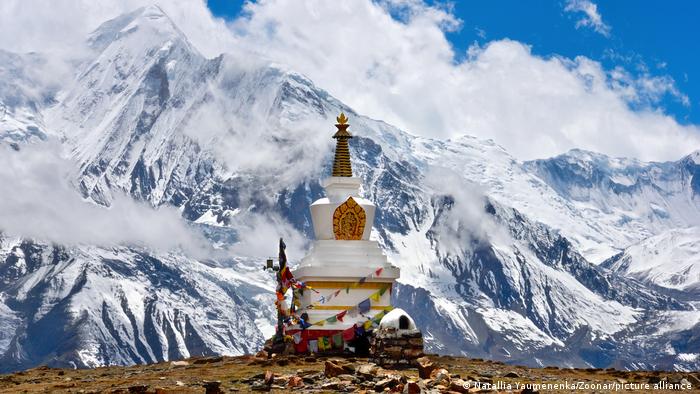 A Buddhist stupa with prayer flags stands in front of the snowy peaks of Annapurna, 4600 meters above sea level