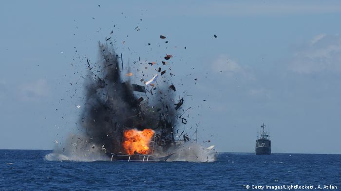 A boat on open water is exploding after being bombarded by a Indonesian navy boat (seen in the background)