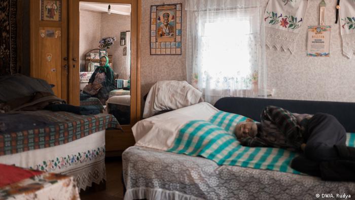 Marusia sits in her home. Her sick husband Ivan lies in bed.