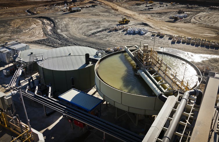 Large outdoor tanks, one filled with a greenish fluid, at a mineral processing plant.