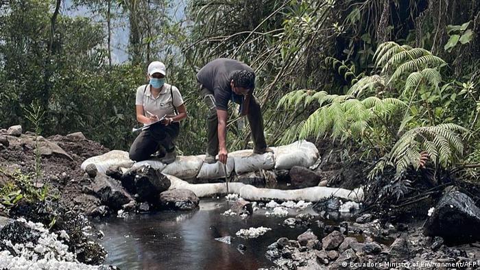 Two people take samples from an oil-contaminated river in Piedra Fina, Ecuador