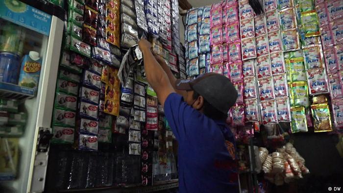A man tears small sachets of produce that hang from long strips in a shop