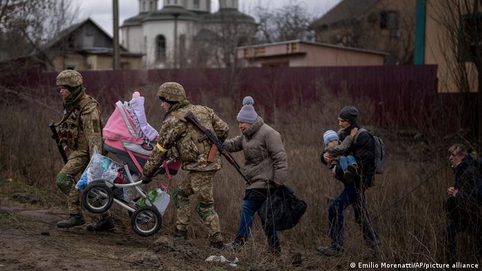 Russia Ukraine War, two soldiers carry as baby carriage, three women walk behind them in a residential neighborhood 