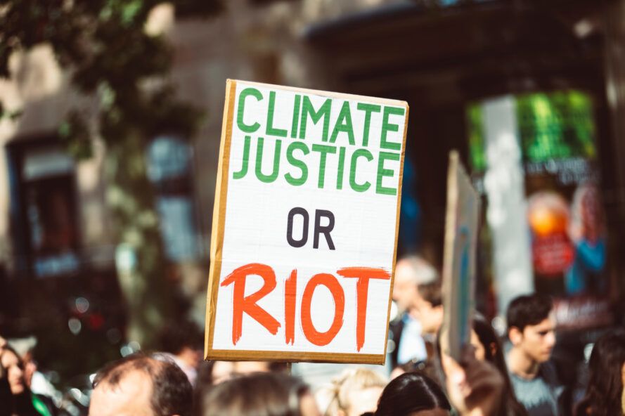 A protest sign reading "climate justice or riot."