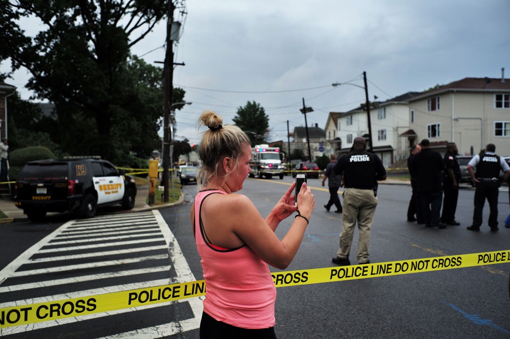 A woman takes pictures with her phone as law enforcement officers secure the area.