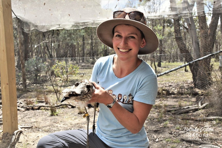 ANU researcher Shoshana Rapley holds bird in hat in an animal enclosure