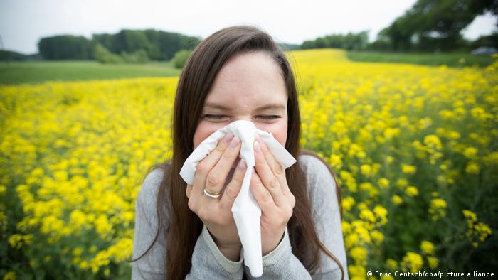 A lady in a field of flowers sneezing into a tissue