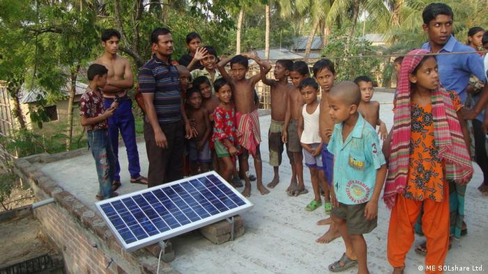 Adults and children with a microgrid solar panel on a flat roof in Bangladesh