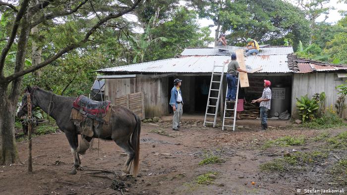 A horse stands in front of a farmer's house in Miraflores in Nicaragua as electricians sets up solar panels on the roof.