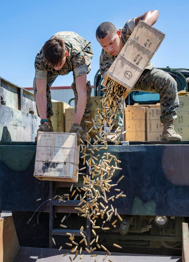 Marines pour boxes of empty brass shell casings into a...