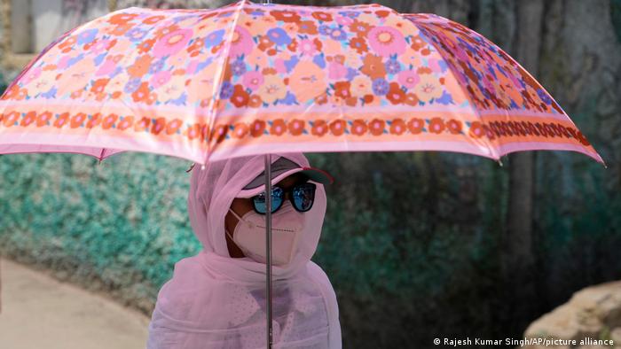 A schoolgirl holds an umbrella and covers herself with a scarf as protection from the sun