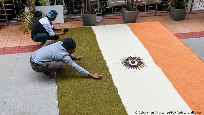 Two men create an Indian flag on the ground using rice and lentils
