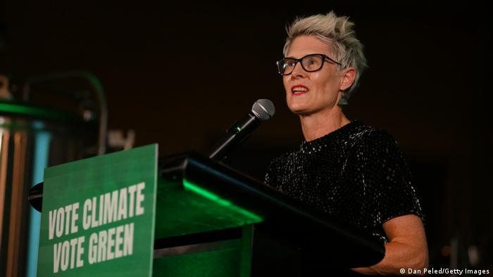 A woman stands in front of a podium. A sign on the podium reads: Vote Climate, Vote Green