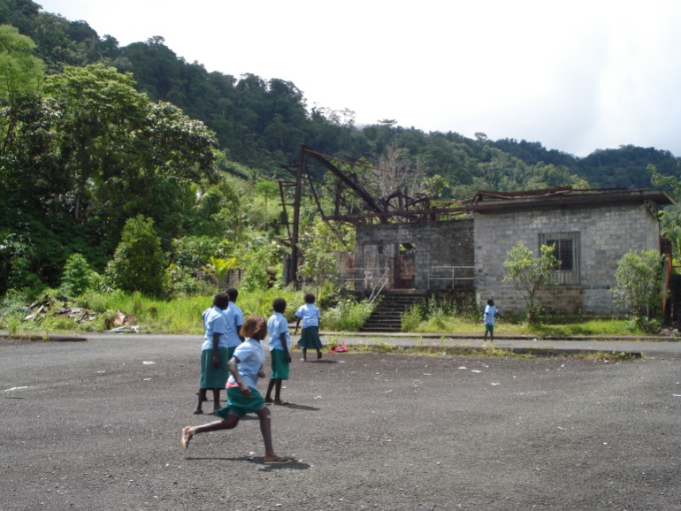schoolgirls in pale blue uniforms play amid the ruined buildings of the panguna mine