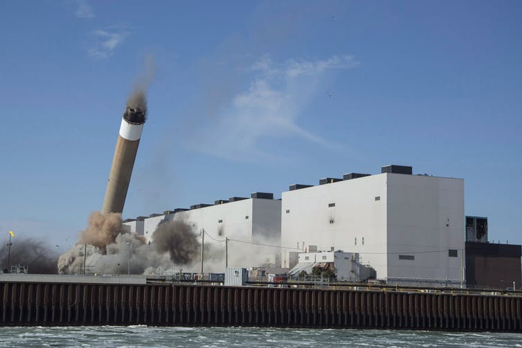 A large white low-rise building with a smoke stack mid-fall.