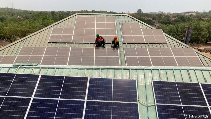 Solar panels and workers on a steep roof in Ghana